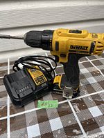Photo of DeWalt 12V cordless drill, battery attached, and charger on checkered surface.