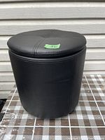 Black faux leather cylindrical foot stool with stitched circular lid closed, showing the exterior.
