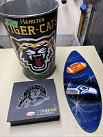 Photo showing full view of Hamilton Tiger-Cats metal trash can, Tim Hortons Tiger-Cats collectible box, and Seattle Seahawks wall plaque