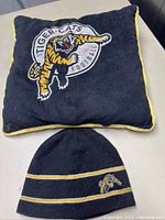 Photo showing the black cushion with the Hamilton Tiger-Cats logo embroidered on the front and the matching black tuque with stripes and logo.