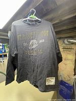 Full front view of the black Hamilton Tiger-Cats long sleeve shirt hanging on a blue hanger showing text and logo