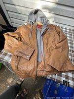 Brown leather ladies jacket with visible zipper pocket and zip cuff detail laid flat with removable grey fabric hoodie attached.