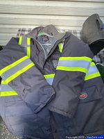 View of the coat front showing dark fabric with two-tone reflective yellow and gray stripes on sleeves and body section.