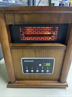 Front view of NOMA heater inside oak wood case showing glowing heating element behind grille.