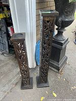 Pair of two tall carved wood candle holders shown standing side by side on outdoor surface, featuring intricate cut-out patterns on sides and square tops.