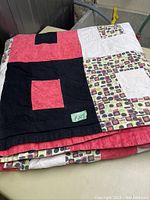 Folded patchwork quilt showing large blocks of red, black, and patterned fabric with geometric designs.