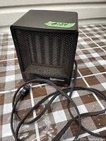 Front view of the small black Super Furnace electric heater showing the mesh protective grille, red indicator light, and power cord coiled in front.