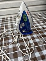 Side view of T-FAL Ultra Glide Pro steam iron showing blue water reservoir, white handle, and attached power cord on patterned surface.