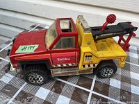 Side view of vintage Tonka tow truck toy showing red cab, yellow tow bed with black and red tow arm, and Tonka branded wheels.