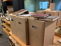 Four banker-style cardboard boxes labeled BOOK and MAG, plus additional repurposed boxes filled with books