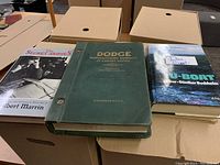 Five boxes of books with various titles including history, automotive, and novels on top.