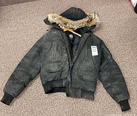 Full view of black Canada Goose parka laid flat showing front, hood and pocket details with paint-like stains