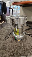 Front view of stainless steel juicer showing housing, power cord, rubber feet