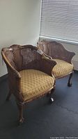 Two matching wooden armchairs with double cane wrapping on backs and sides. Upholstered gold patterned seats. Chairs have carved claw feet and decorative wood detailing.