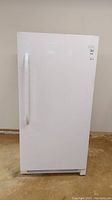 Full front view of white upright freezer with handle and manufacturer label.