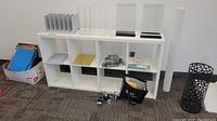 White Ikea office shelf unit with 8 open compartments placed against wall with carpet floor. Accessories shown in photos are excluded from sale.