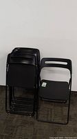 Six black Ikea Nisse folding chairs shown stacked and standing next to each other.