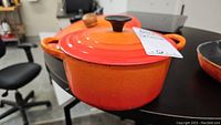Side view of orange Le Creuset Dutch oven with lid on black surface in office environment