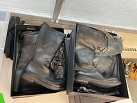 Two open shoeboxes each containing a pair of black leather boots on a table