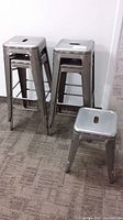 7 stackable metal stools with silver metallic finish, square seats with handle cut-out.
