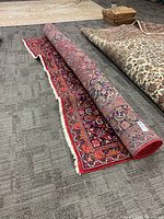 Rolled red-field rug partly unrolled to show overall pattern