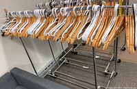 Overall view of metal clothes rack loaded with many wood and plastic hangers in white and natural wood color, showing rack's frame and casters.