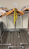 Metal clothes rack with various wooden, plastic, and metal hangers hung along the bar, with a yellow measuring tape hanging on one side.