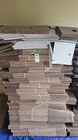 Stacks of flattened shipping boxes piled high against a wall, showing differing sizes and colors.
