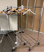 Two chrome metal clothes racks on casters with wood, plastic, and metal hangers in white, black, and natural wood.