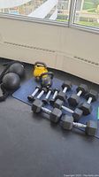 All weights on foam flooring by window: two medicine balls with rope, kettlebells, dumbbells.