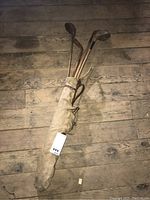 Full view of vintage canvas and leather golf bag holding four hickory shaft golf clubs.