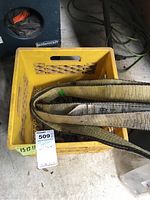 Yellow milk crate on the floor containing a folded heavy-duty yellow and black towing strap and rusty metal towing chain links.
