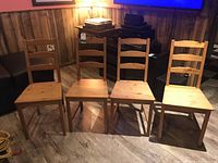 Four wood veneer IKEA Jokkmokk chairs arranged in a row, showing the front and side angles with wear consistent with age.