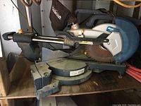 Side view of Mastercraft 10 inch compound miter saw showing blade guard and sliding rails with dust and wear.