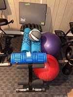 Marcy adjustable weight bench with blue yoga mats, small grey and black medicine ball, purple and red exercise balls, and blue foam roller on carpeted floor.