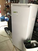 Front view of white Frigidaire upright freezer with top handle, placed in a shed environment, showing some wear and a sticker on the door.