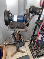 Front view of the Mastercraft bench grinder mounted on a rusted stand in a shed environment with cable and nearby shelving.