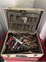 Open metal carrying case filled with assorted used hand tools including screwdrivers, pliers, and various socket tools.