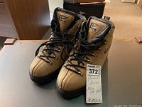 Pair of tan brown and black Nike Air hiking boots displayed side by side with a lot tag attached to one boot.