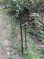 Two iron tools standing outdoors surrounded by grass and plants, a long rod and a smaller curved pry bar visible