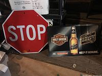 Red octagonal stop sign next to rectangular Harley Davidson/Miller Genuine Draft sign on wooden floor.