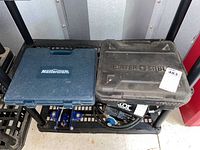 Blue Mastercraft plastic case and black Porter-Cable plastic case side by side on a metal rack.