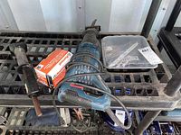 Bosch RS7 reciprocating saw with Ramset punch HD22, Ramset fasteners in box, spare saw blades in plastic container, and spade drill bits on plastic shelving rack.