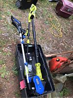 Tools including electric snow shovel, weed trimmer, pole saw and storage bin shown on ground