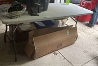 Full side view of the white folding table showing its collapsible metal legs and supporting braces beneath the tabletop.