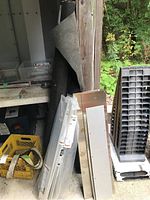 Photo showing roll of black weed barrier fabric leaning against wall next to metal threshold strips and kick plates stacked neatly.