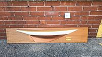 Front view of the mounted wooden half-hull model of the Gloriana yacht on a wooden plaque.