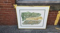 Framed abstract expressionism lithograph artwork leaning against brick wall.