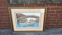 Framed Venice canal art print showing a bridge over a canal with a gondola in the water, against a brick wall background.