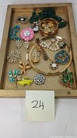 Top-down view of all costume jewelry including diverse brooches, necklace, and rings arranged on a wooden tray